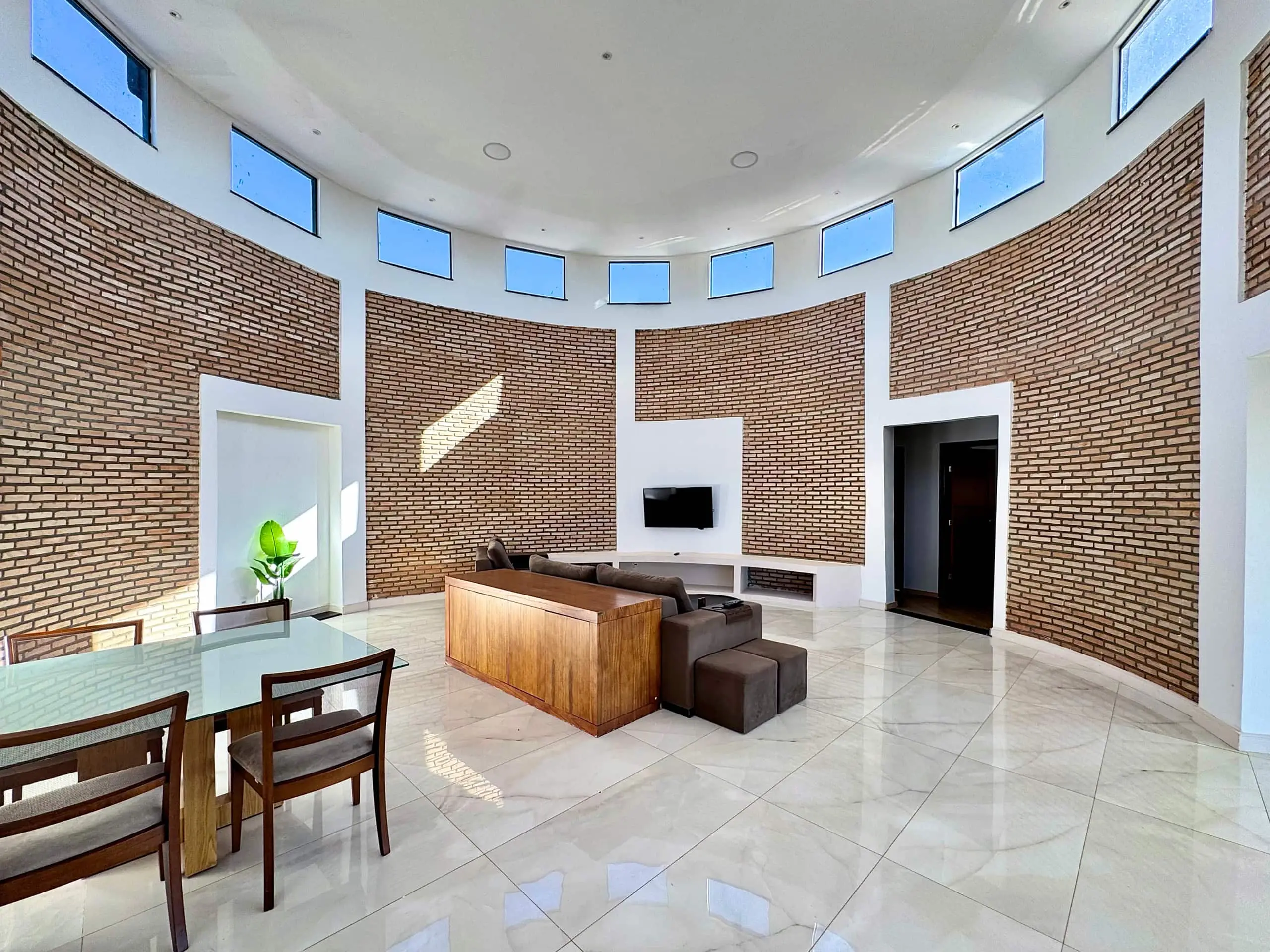 Sala de estar ampla, com parede curva de tijolo aparente e piso de mármore.