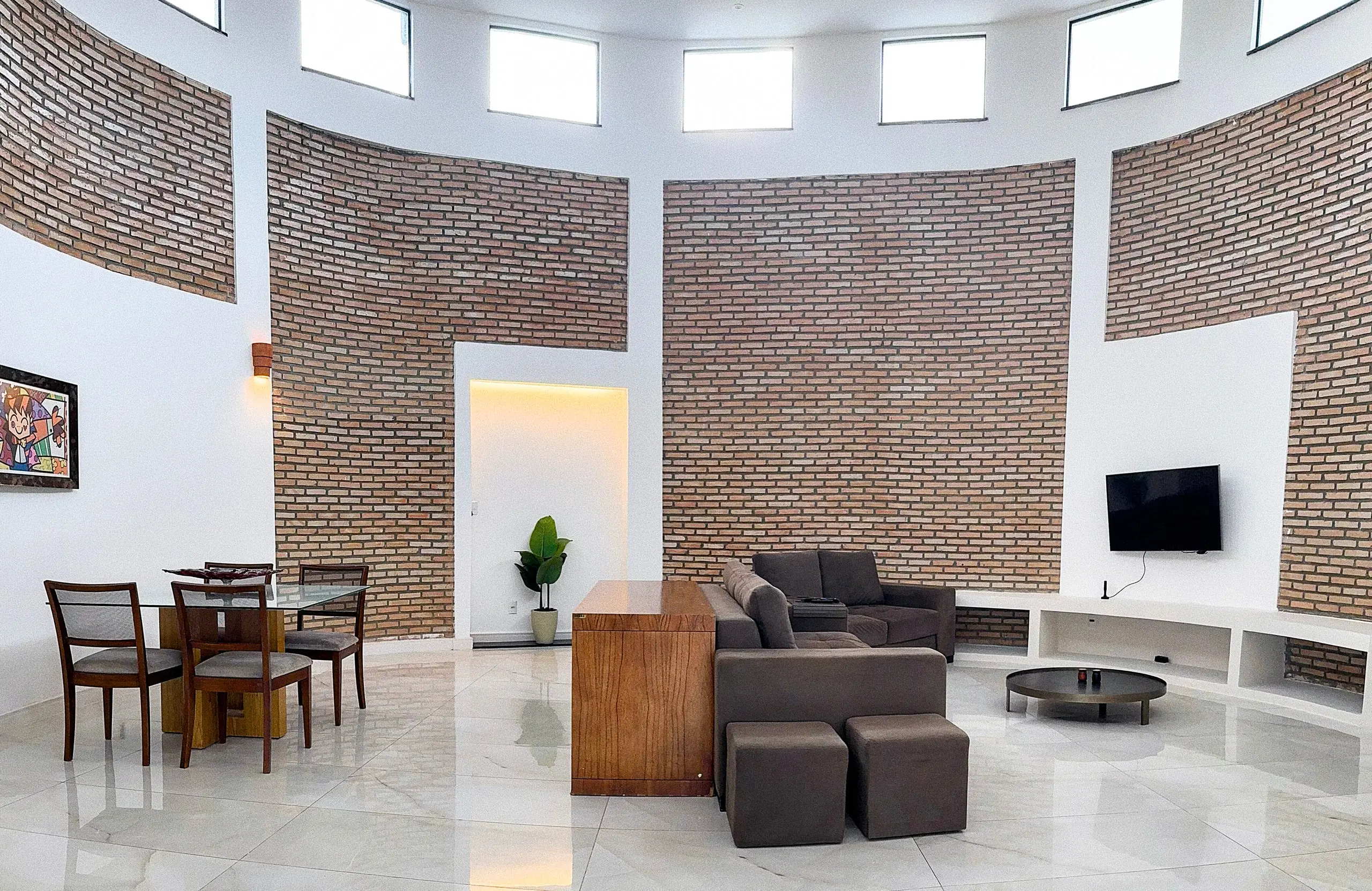 Sala de estar ampla, com parede curva de tijolo aparente e piso de mármore.